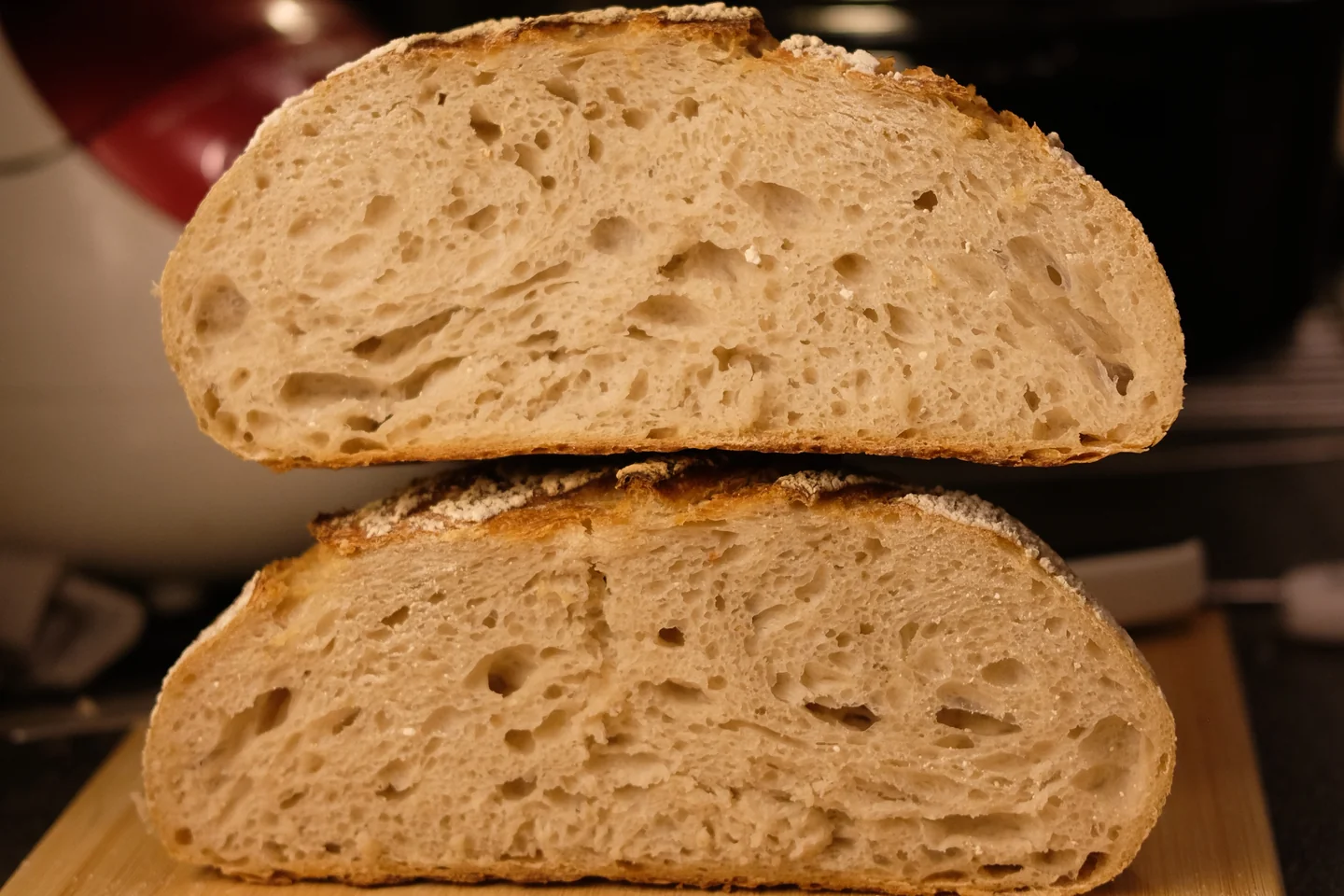 Two halves of a cut sourdough loaf stacked on a wooden board, showing an open, airy crumb